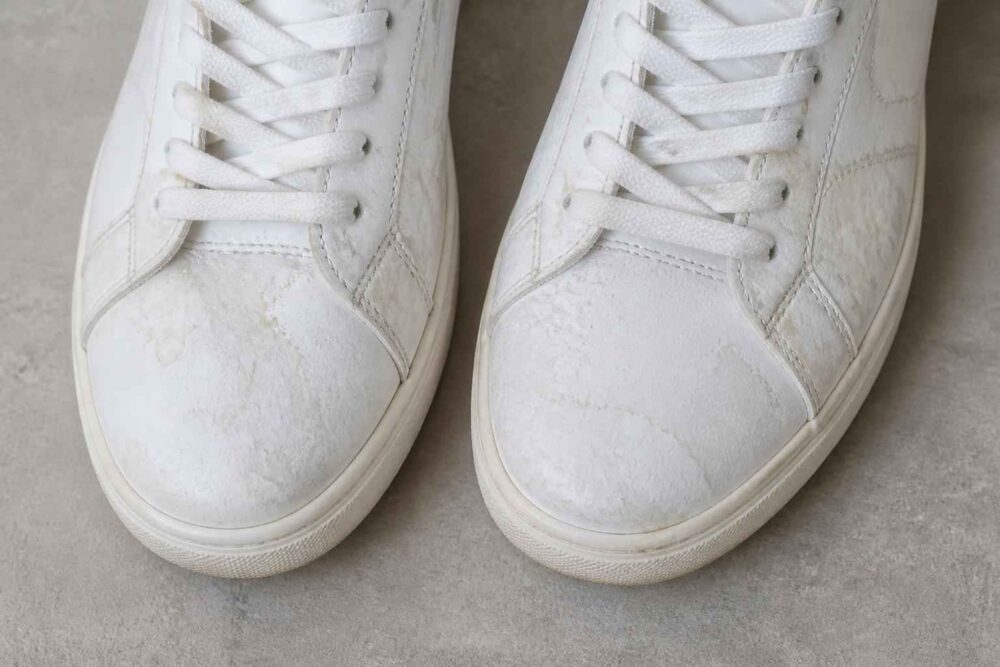 Zbliżenie na parę białych sneakersów z widocznymi śladami zużycia na noskach i sznurówkach