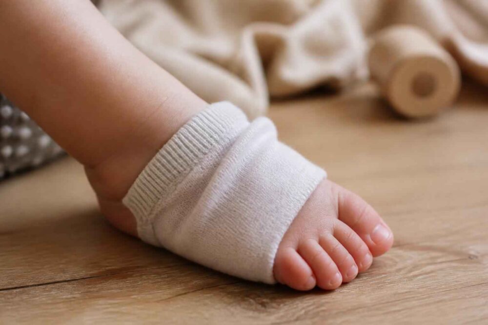 Stopa małego dziecka w białym opatrunku na drewnianej podłodze